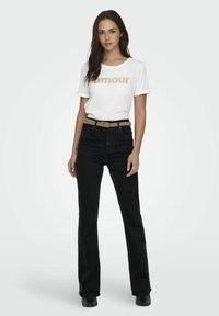 Vit t-shirt med "amour" i guldglitter, kombinerad med högmidjade svarta jeans och ett flätat beige bälte. Svarta ankelskor fulländar stilen.