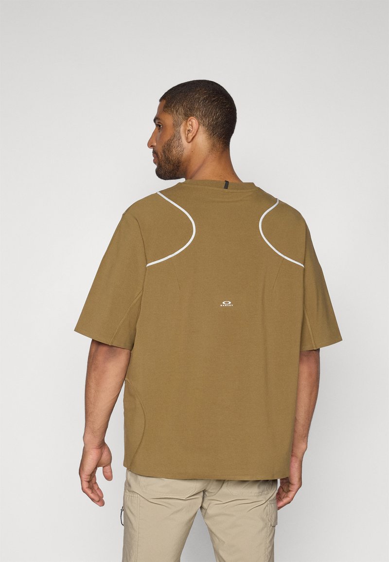 Brun kortärmad t-shirt med vita detaljer, rund halsringning och etikett på baksidan. Tyget verkar mjukt med en avslappnad passform och subtil logotypdetalj.