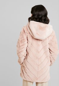 Chaqueta de pelo sintético rosa claro con capucha, que presenta una textura en zigzag y un corte relajado. La tela parece suave y esponjosa.