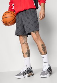 Nike grå basketballshorts med et geometrisk mønster, kombinert med svarte og hvite sneakers og hvite sokker, holder en oransje basketball.