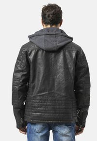 Zwarte leren jas met doorgestikte details op de schouders en rug, ritszakken, en een grijze capuchontrui eronder.