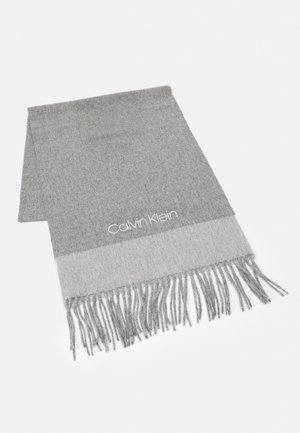 Écharpe grise en tissu doux, avec une bordure gris clair et des franges à une extrémité. Logo "Calvin Klein" brodé en blanc.