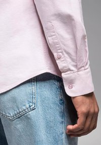 Lichtroze overhemdbloes met lange mouwen, voorzien van een afgeronde onderrand en knopenmanchetten, gecombineerd met lichtblauwe denim.