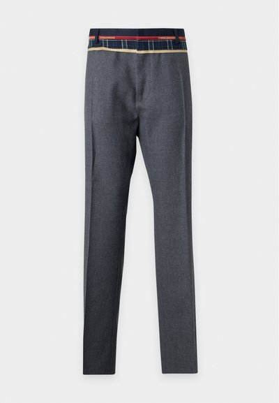 Pantalon gris sur mesure avec une ceinture à carreaux comportant des détails rouges et bleu marine et un texte sur fond blanc uni.