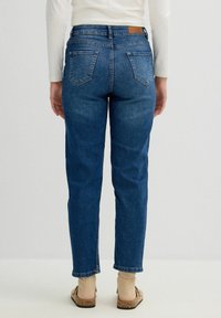 Jeans de mezclilla azul oscuro con un ajuste regular, pierna recta, que cuentan con bolsillos traseros y un parche de cuero marrón en la cinturilla.
