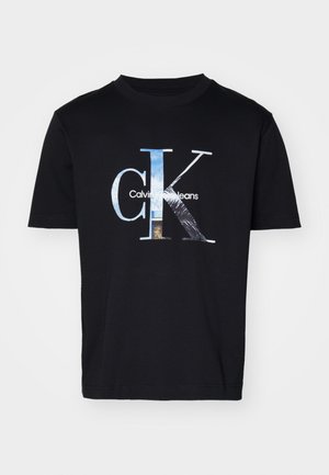 T-shirt en coton noir avec un logo graphique texturé portant le texte "Calvin Klein Jeans" et un design stylisé "CK" en nuances de bleu et d'argent.