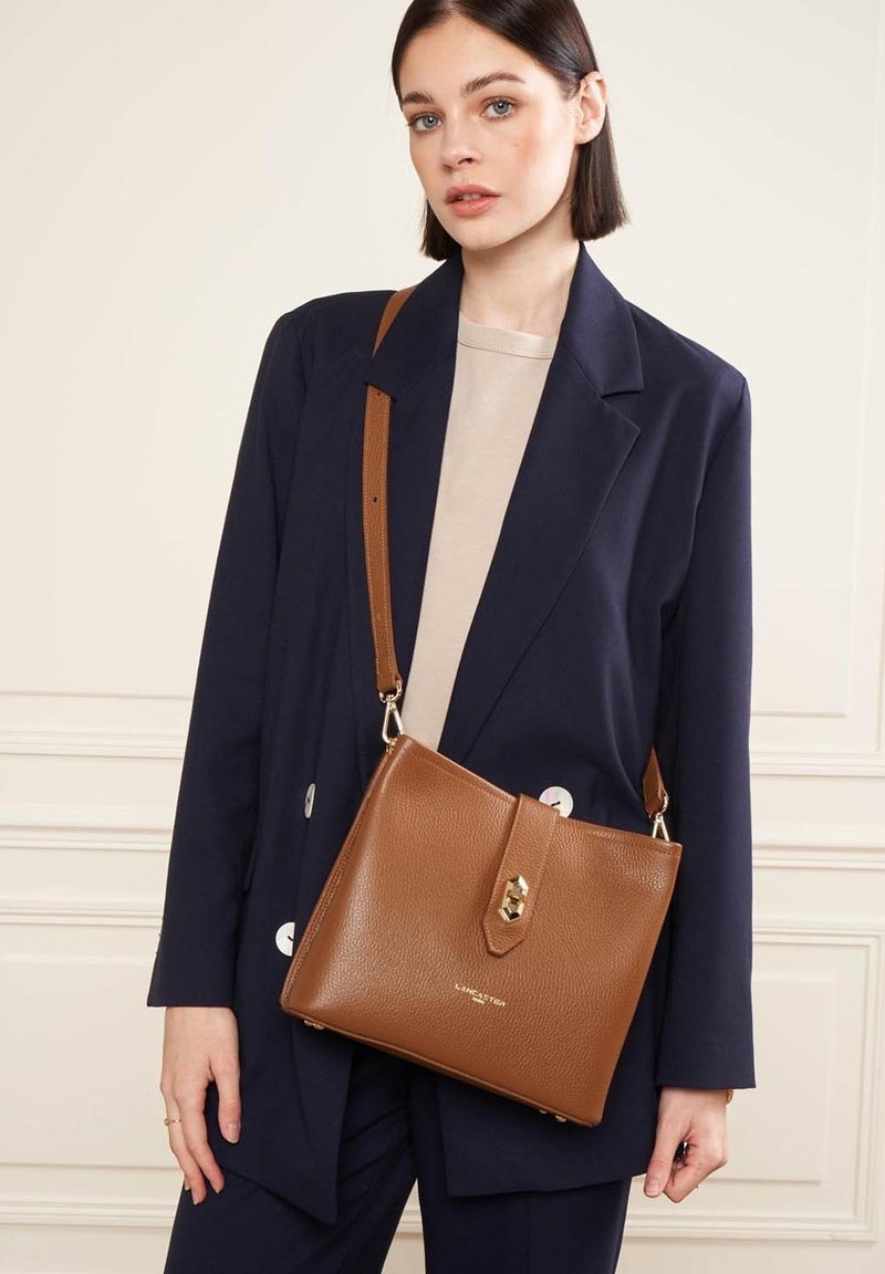 Borsa a spalla in pelle marrone con texture, chiusura a pattina e dettagli in oro, dotata di una tracolla regolabile e un design rettangolare elegante.