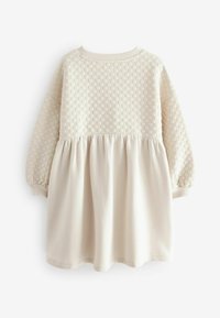 Beige mekko, jossa on teksturoitu yläosa, jossa on geometrinen kuvio, pitkät hihat ja sileä, rypytetty alaosa. Puuvilla-sekoitemateriaali.