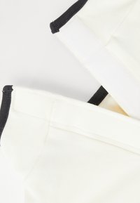 Dwa kremowe paski z tkaniny z czarnymi krawędziami i teksturowanym zapięciem na rzepy. Materiał wydaje się miękki i rozciągliwy, z starannymi detalami szwów.