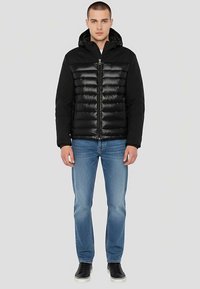 Sort pufferjakke med hætte, med quiltet tekstur, lynlås og kontrastfarvede ærmer. Kombineret med blå jeans og sorte sneakers.