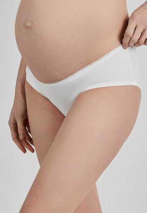 Rase perioodil olev inimene kannab valgeid rasedatele mõeldud aluspesu, käsi tõmbab õrnalt pükste vööd kõhust eemale.