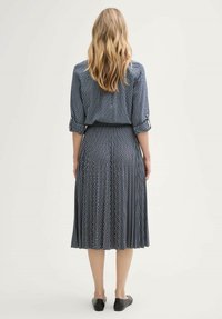 Bla dresses mit einem gemusterten Design, einem gefälteten Rock, langen gesmokten Ärmeln und einer taillierten Taille. Getragen mit schwarzem Schuhwerk.