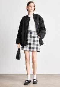 Μαύρο bomber μπουφάν, άσπρη στενή μπλούζα, καρό μίνι φούστα σε μαύρο και άσπρο, κρατώντας μια μικρή μαύρη τσάντα, φορώντας άσπρες κάλτσες και μαύρες γόβες.