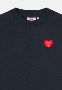 Mørkeblå crewneck sweatshirt med ribbestrikket krage og rød hjerteapplikasjon på venstre bryst med teksten "THE V.I.P CLUB".