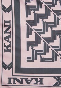 Zīda šalle ar ģeometrisku melnu rakstu uz maigi rozā fona, ko ieskauj šaura melna apmale ar vārdu "KANI".
