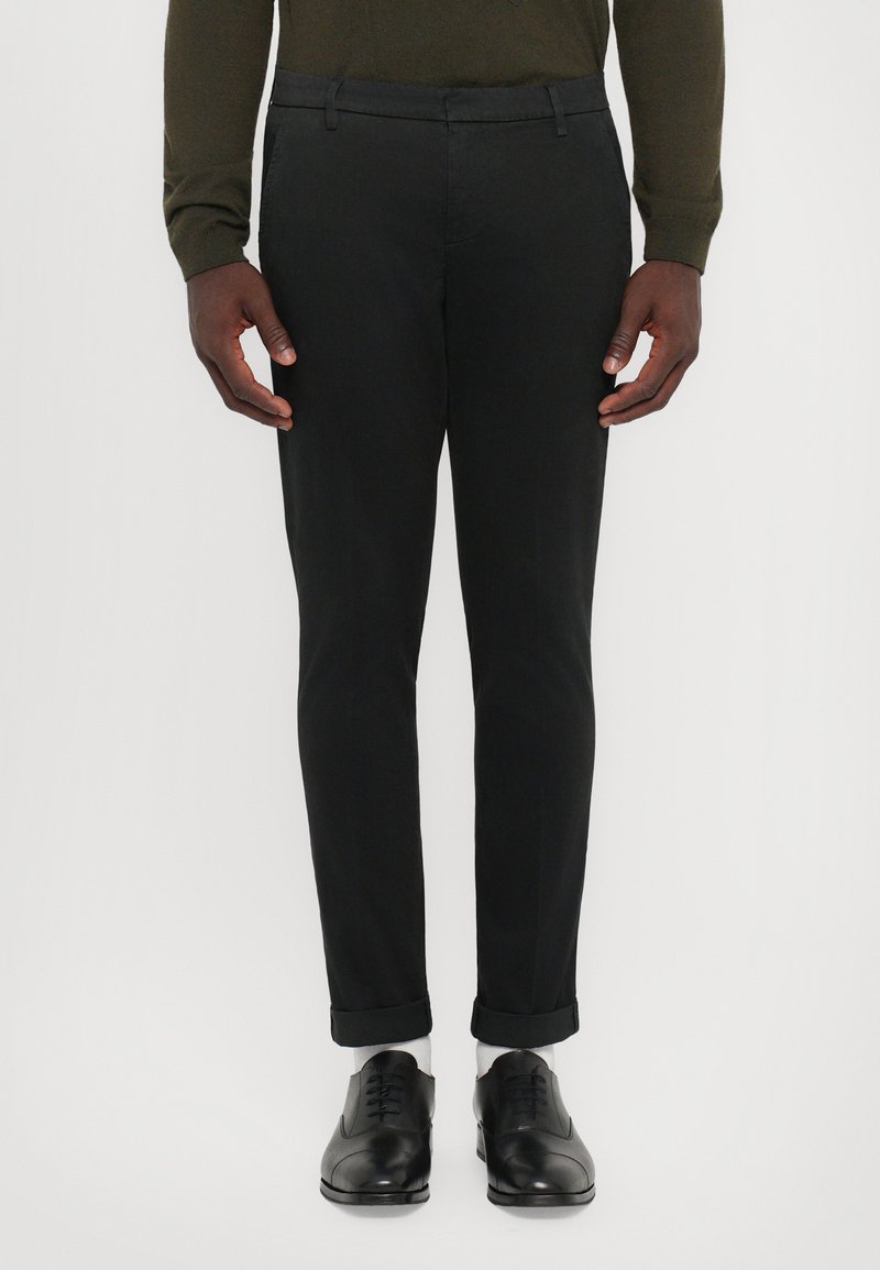 Pantaloni neri su misura con una vestibilità slim, caratterizzati da una texture liscia, orli arrotolati e una parte frontale piatta. Indossati con scarpe eleganti nere.