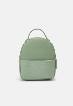 Sac à dos en cuir synthétique vert avec des accents en croco texturé, forme arrondie en haut, fermeture éclair et une poignée supérieure. Design compact et structuré.