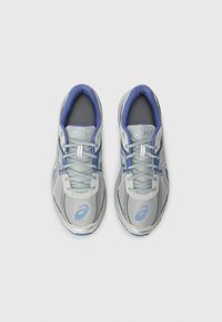 Ζευγάρι γκρι και μπλε αθλητικών παπουτσιών Asics με κορδόνια, από επάνω, σε λευκό φόντο.