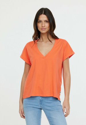 T-shirt orange à manches courtes avec un col en V, fabriqué en coton, avec des manches retroussées et un ourlet droit, associé à un jean bleu clair.