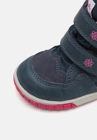 Blaues Wildleder- und synthetisches Knöchelschuhmodell mit pinken Akzenten, zwei verstellbaren Klettverschlüssen und einer strukturierten Gummisohle.