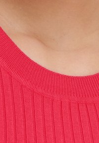 Gros plan sur le cou et le haut de la poitrine d'une personne portant un pull côtelé rose vif à encolure ronde.