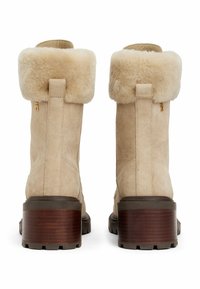 Botas de tobillo de ante beige con un puño esponjoso de color crema, tacones texturizados marrones y detalle de cremallera lateral; diseño robusto y casual.