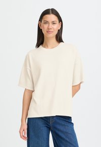 T-shirt en coton beige oversize avec col rond, manches courtes et coupe décontractée. Texture lisse, détails de couture minimalistes.
