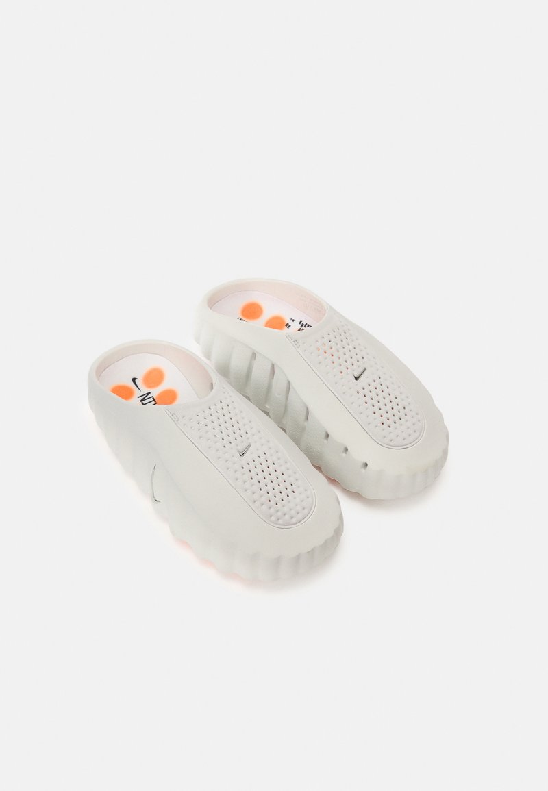 Mules gris clair avec un design perforé, des bords arrondis et une semelle texturée. Doublure intérieure douce avec des accents orange et un détail de logo.