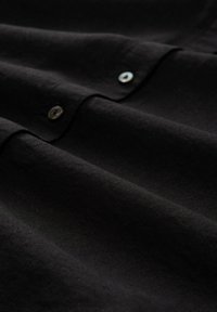 Tessuto nero con una consistenza liscia, caratterizzato da pieghe visibili e due bottoni rotondi e lucidi lungo il bordo.