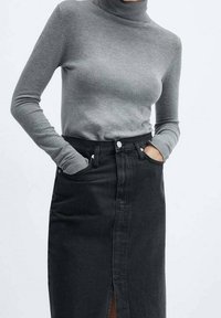 Suéter gris de cuello alto con mangas ajustadas, combinado con una falda de mezclilla negra de tiro alto que presenta una abertura frontal y bolsillos.