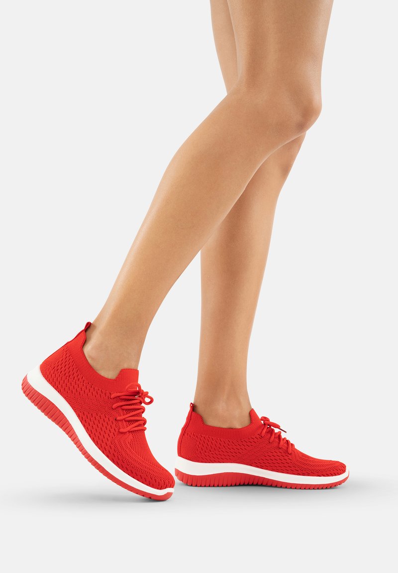 Des baskets tricotées rouges avec un haut texturé, un système de laçage et une semelle intermédiaire blanche avec un motif ondulé. Conception légère et flexible.