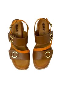 Sandali in pelle marrone con dettagli arancioni, dotati di due cinghie larghe e accessori circolari dorati. Suola piatta con una leggera texture. Fabbricati in Italia.