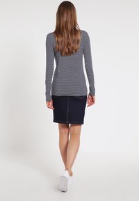 Top de manga larga a rayas en blanco y negro combinado con una falda de mezclilla oscura, con costura trasera y diseño a la altura de la rodilla. Llevado con zapatos blancos.