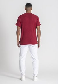 Červené krátke tričko s rebrovaným vzorom a okrúhlym výstrihom, skombinované s bielymi nohavicami s rovnými nohavicami a bielymi teniskami, z pohľadu zozadu.