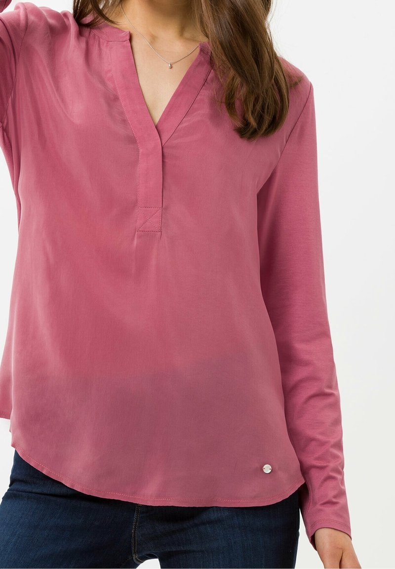 Camicia a maniche lunghe rosa chiaro con scollo a V, texture sottile e un accento di bottone argentato all'orlo. Tessuto liscio con una vestibilità rilassata.