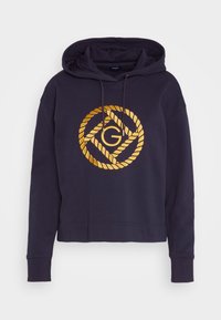Sudadera corta de color azul marino con un logo de diseño en forma de cuerda dorada que presenta una "G" interconectada en el centro. Tejido de mezcla de algodón con capucha ajustable.