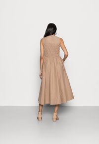 Beiges ärmelloses Kleid mit einem gerafften Rücken, knielangem Rock und tailliertem Oberteil. Glattes Material und klare Linien heben das Design hervor.