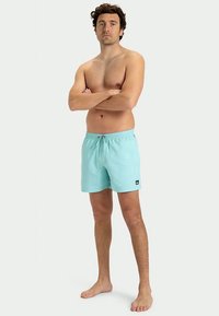 Τυρκουάζ μαγιό κατασκευασμένα από ελαφρύ ύφασμα, με ελαστική ζώνη στη μέση, κορδόνι και ένα μικρό μαύρο λογότυπο στο μπροστινό μέρος.