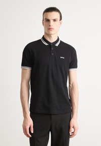 Schwarzes Poloshirt mit kontrastierenden Kragen- und Ärmelakzenten. Verfügt über drei Knöpfe und ein kleines "BOSS"-Logo auf der Brust. Glatte Textur.