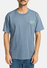 Cotton blue t-shirt featuring a green embroidered eye logo and text on the left chest. Short sleeves and a classic round neckline.