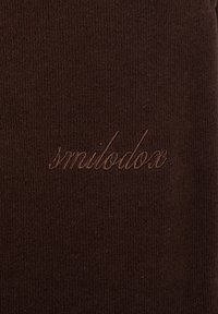 Braunes Strickgewebe mit "smilodox" in passendem dunkelbraunem Garn in Schreibschrift gestickt.