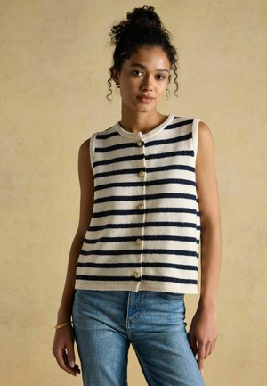 Marineblau-weiß gestreConttes ärmellose Strickweste mit goldenen Knöpfen, getragen über hellblauen Jeans. Weiche Textur und leicht verkürzter Schnitt.