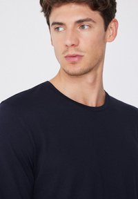 Marineblaue Langarm-T-Shirt aus weichem Stoff mit Rundhalsausschnitt und glatter Textur, ausgestattet mit minimalen Nähdetails.