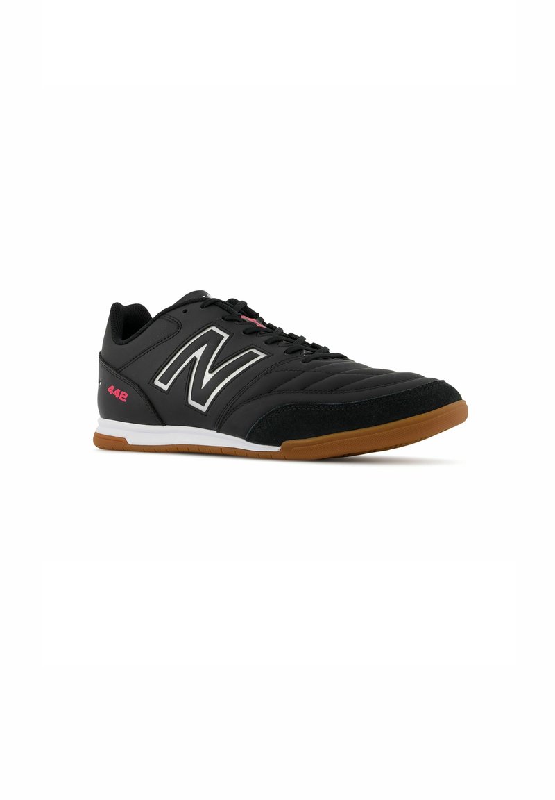 Baskets de sport noires avec un dessus en synthétique texturé, une semelle intermédiaire blanche et une semelle extérieure en caoutchouc caramel. Présente un logo "N" bien visible et un col rembourré.