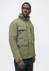 Olivgrüne, isolierte Jacke mit hohem Kragen, mehreren Taschen und Reißverschluss. Verfügt über eine glatte Textur und verstellbare Manschetten.