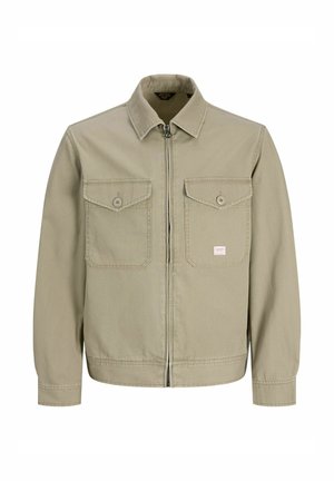 Beige Reißverschlussjacke mit spitzem Kragen, zwei knöpfbaren Brusttaschen, langen Ärmeln und einem kleinen rechteckigen Etikett auf der linken Tasche.