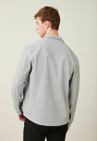 Camisa gris de manga larga con cuello; cuenta con puños abotonados y un dobladillo recto. Tela suave con una textura sutil.