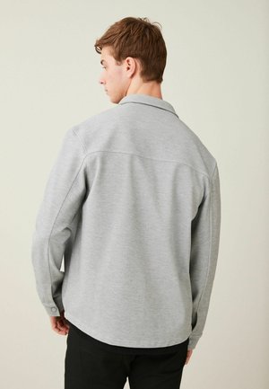 Camisa gris de manga larga con cuello; cuenta con puños abotonados y un dobladillo recto. Tela suave con una textura sutil.