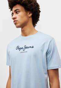 Ανοιχτό μπλε κοντομάνικο μπλουζάκι φτιαγμένο από βαμβάκι, με ναυτικό λογότυπο "Pepe Jeans" και "LONDON" σε κόκκινα γράμματα στο στήθος.