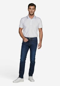 Weißes Poloshirt mit Kragen und marineblauen Akzenten, kombiniert mit dunkelblauen Slim-Fit-Jeans und weißen Sneakers. Das Outfit ist lässig und figurbetont.